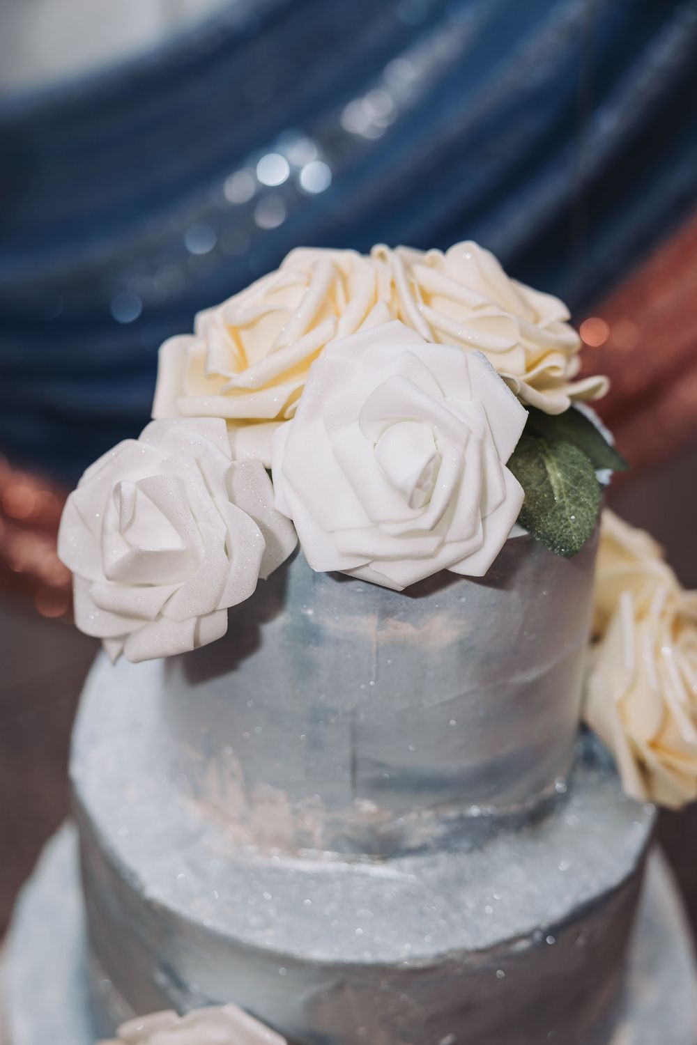 A silver metallic wedding cake decorated with delicate white roses and sparkly details on multiple tiers.