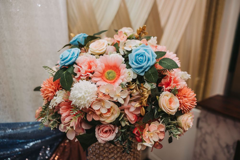 Colorful wedding bouquet with pink, blue and white flowers arranged on a wooden surface in a rustic setting.