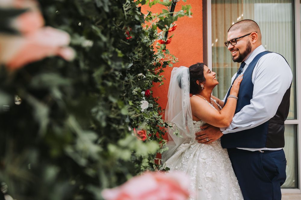 Romantic outdoor wedding couple sharing tender moments in a garden setting with blush pink florals and greenery.