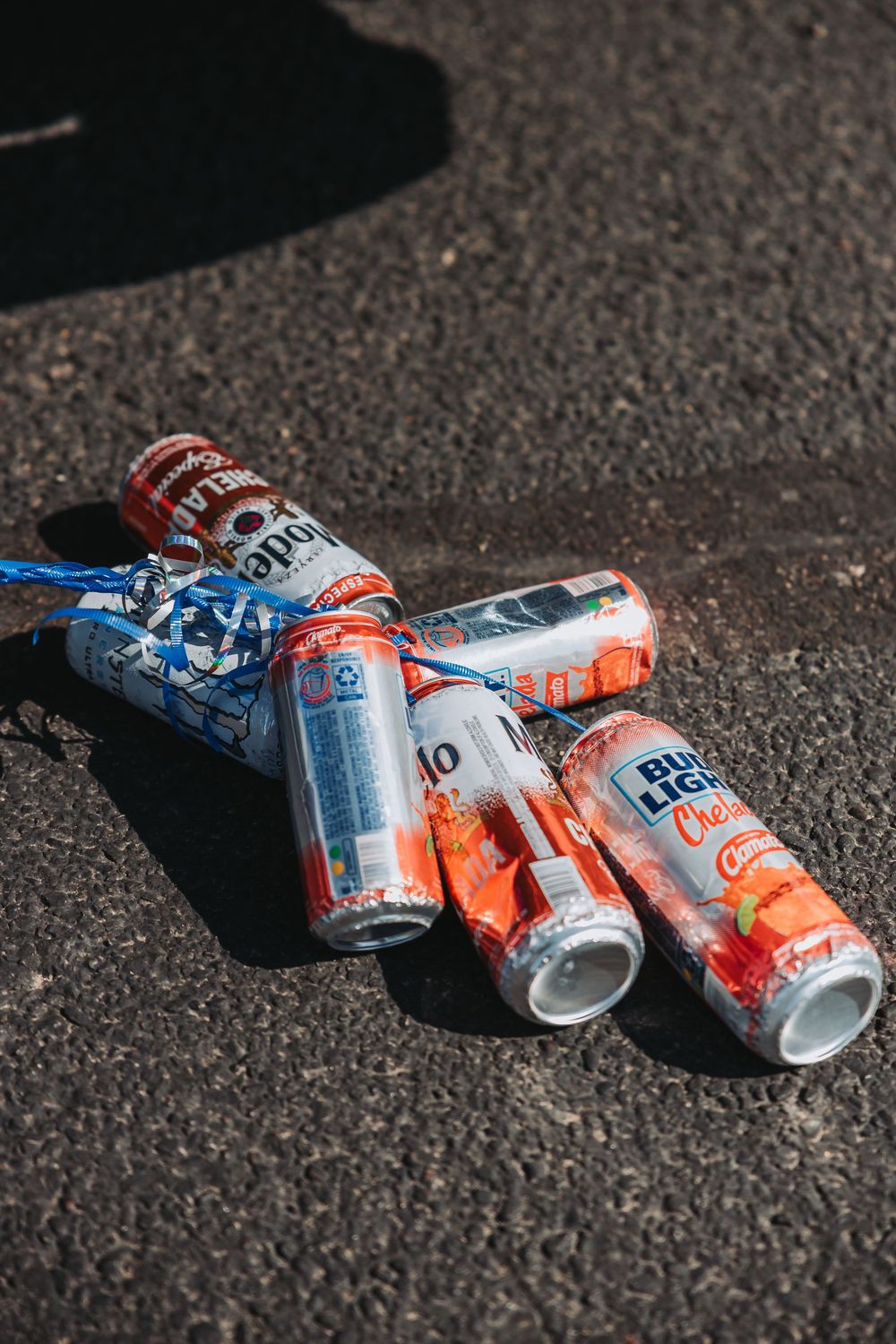 Crushed empty Diet Coke cans scattered on dark asphalt ground in bright sunlight.