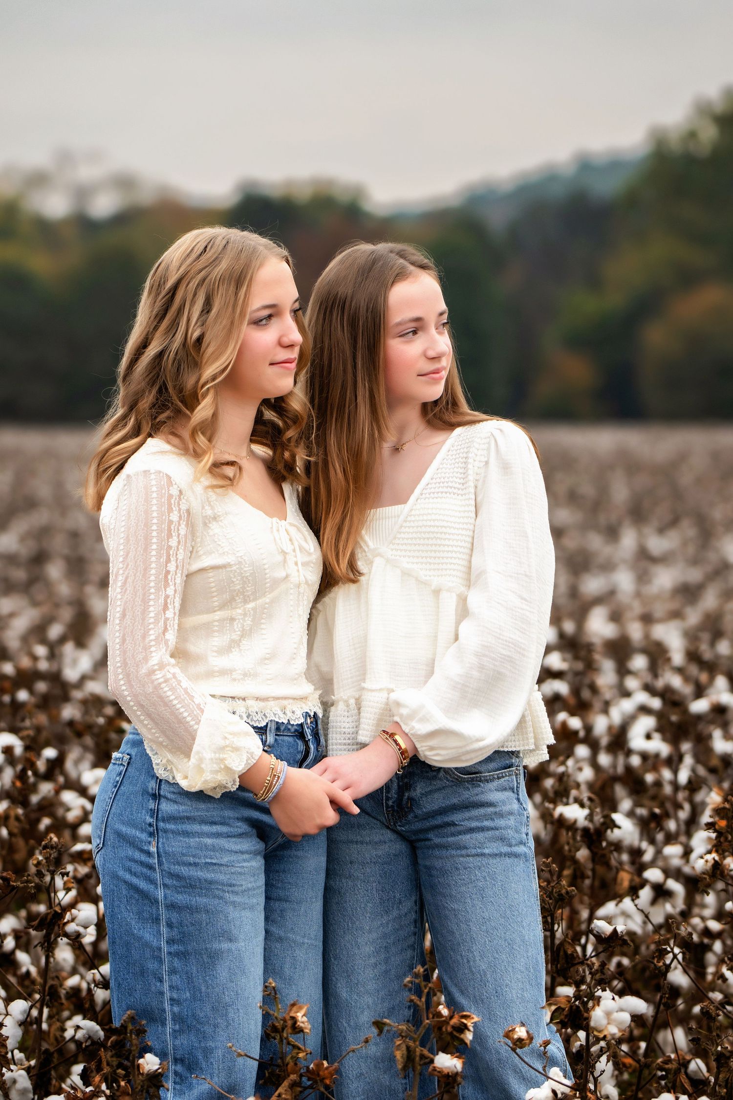 Two sisters in neutral colors holding hands in a cotton field and staring away while doing a photo session in Cartersville Georgia