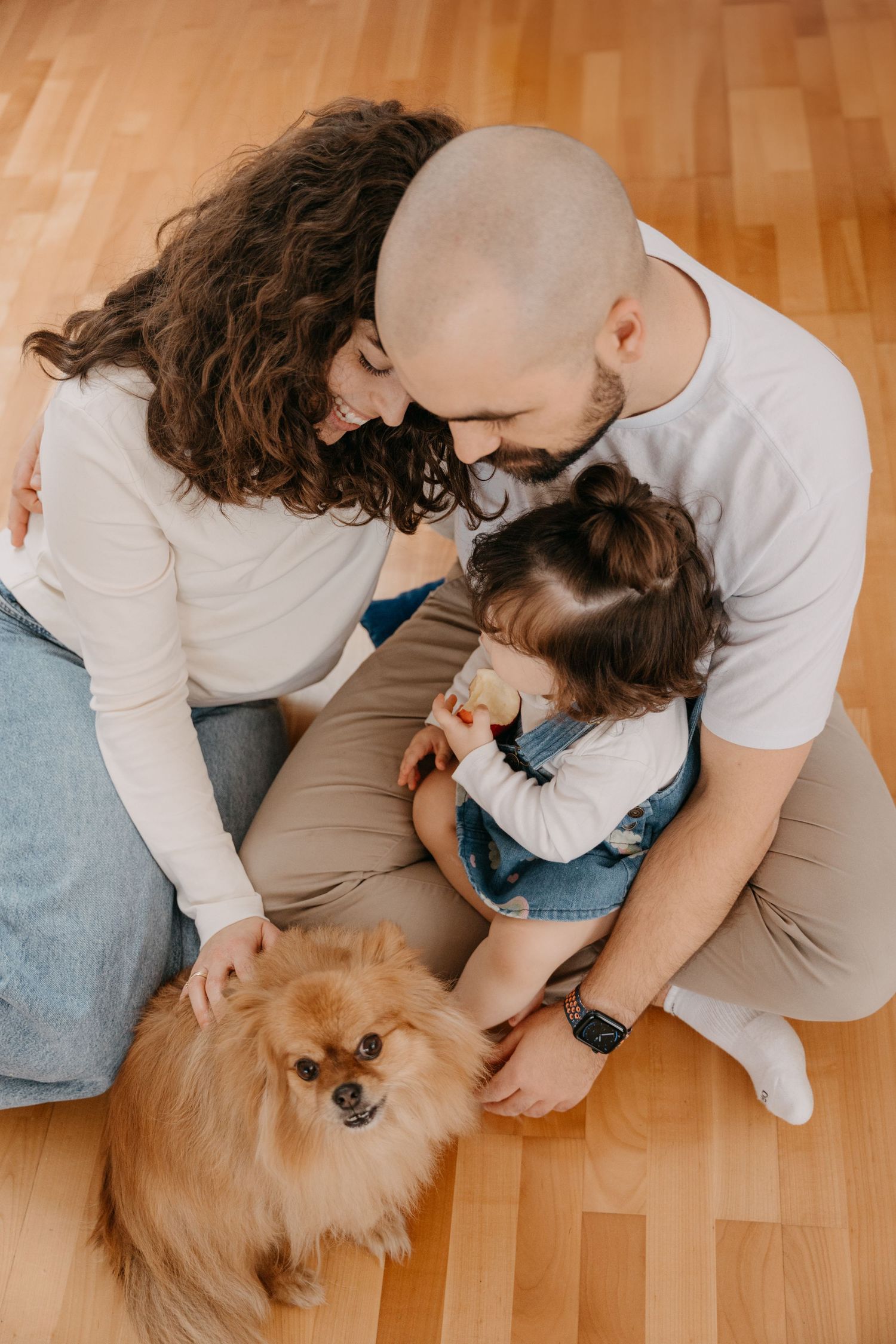A couple sitting on hardwood floor playing with their fluffy Pomeranian dog in a series of candid moments.
