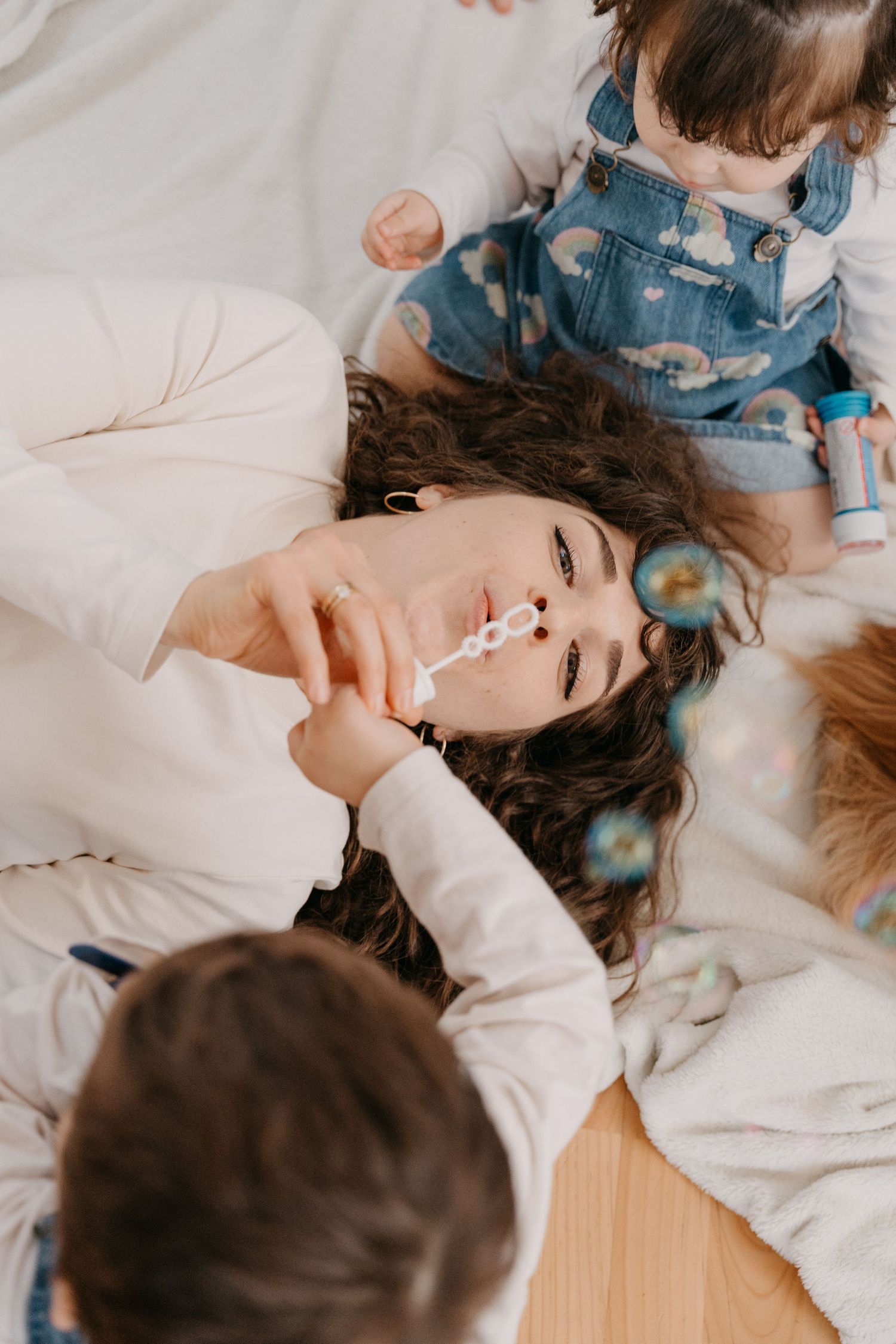 A mother and child share tender moments while lying together on white bedding in a series of intimate portraits.