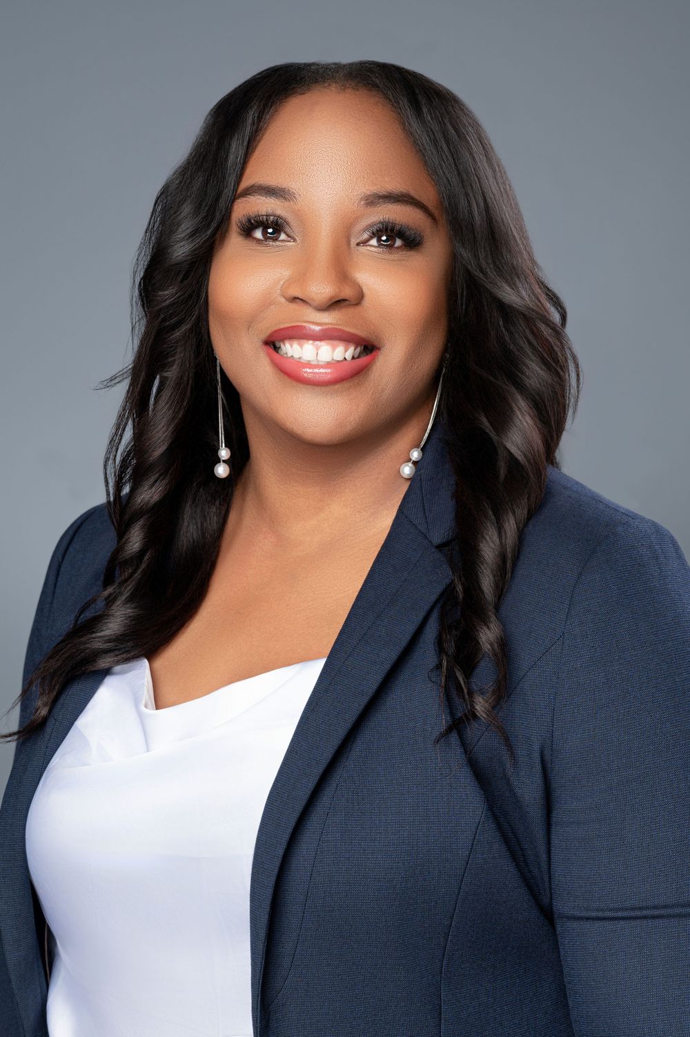 Professional headshot series showing a person in a navy blazer and white top with a bright smile against a gray background.