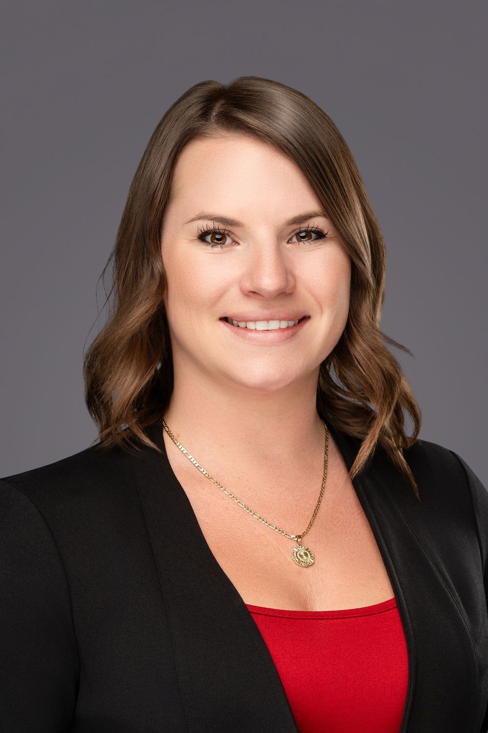 Professional headshot portrait featuring black blazer and red top against gray background.