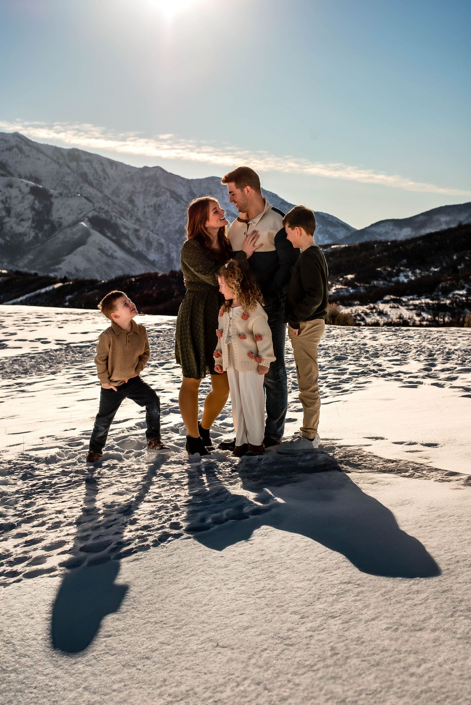 family embracing each other. sun in the backgound with beautiful snow on the mountains and ground at Snowbasin, Utah