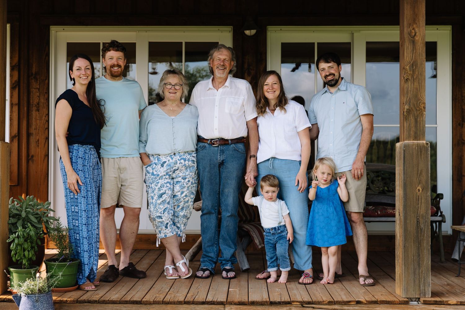 A group of people stand together on a wooden porch of a house during a summer day.