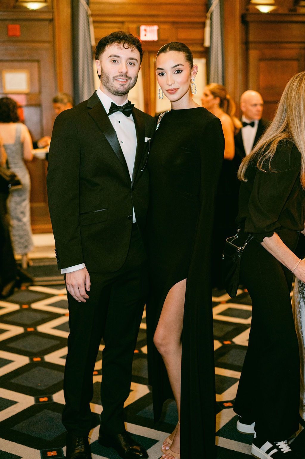 Formal event in an elegant hallway with guests in black tie attire standing against a geometric patterned floor