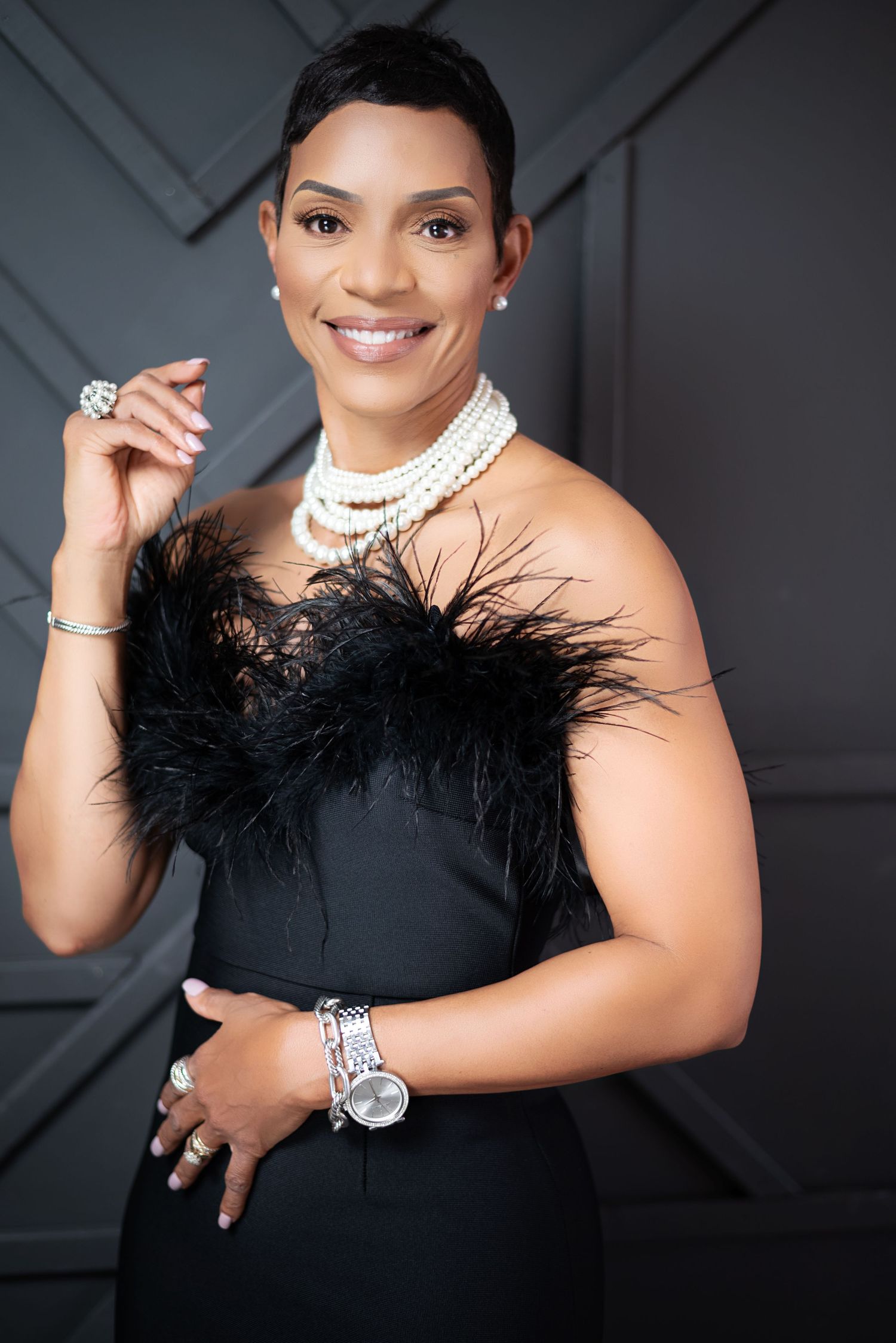 Glamorous studio portrait series featuring elegant black feather details, pearls and formal attire against a gray backdrop.