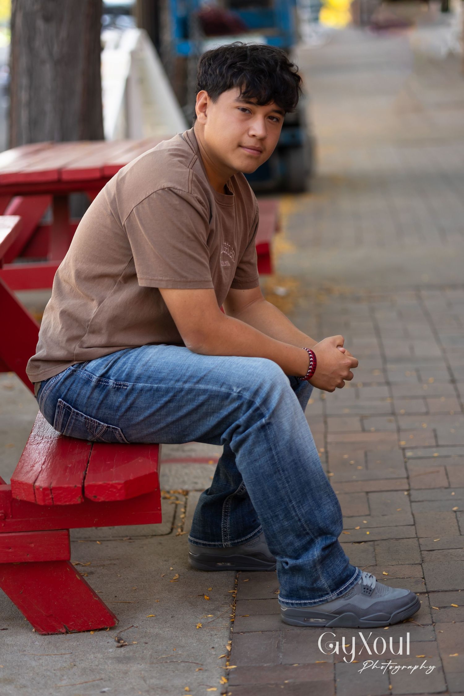 Person in brown polo shirt sitting on red bench on brick sidewalk.