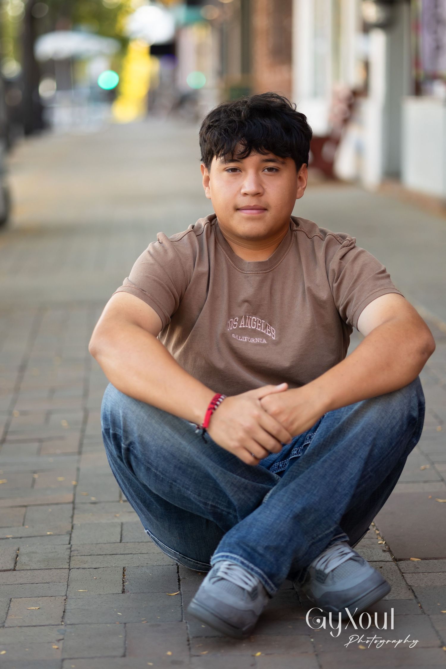 Person in brown t-shirt sitting cross-legged on brick pavement.