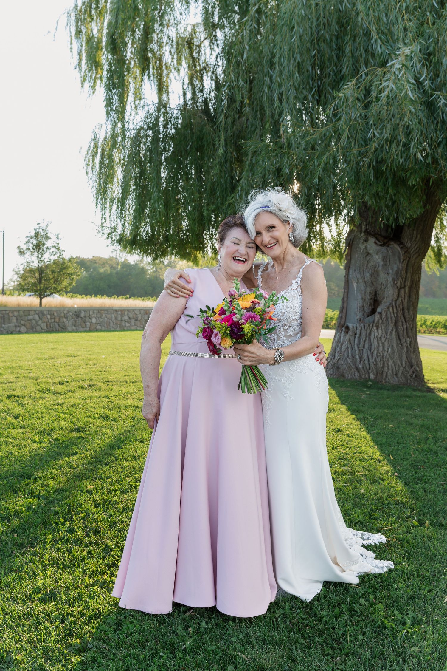 Bride and her mom share a hug under the grand willow tree at Vineland Estates Winery.