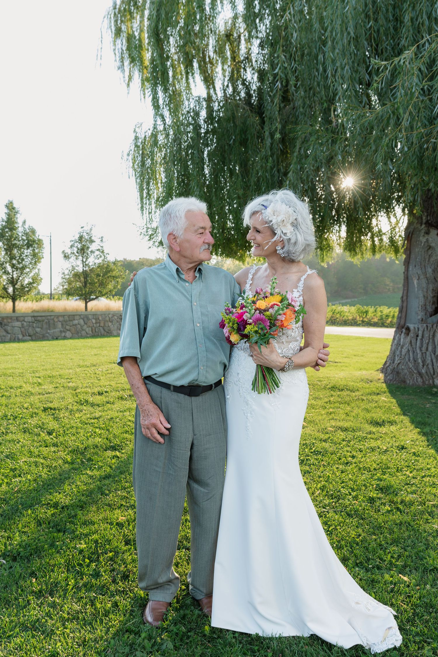 A tender moment of a bride and her dad under a weeping willow tree with vibrant flowers at Vineland Estates Winery.