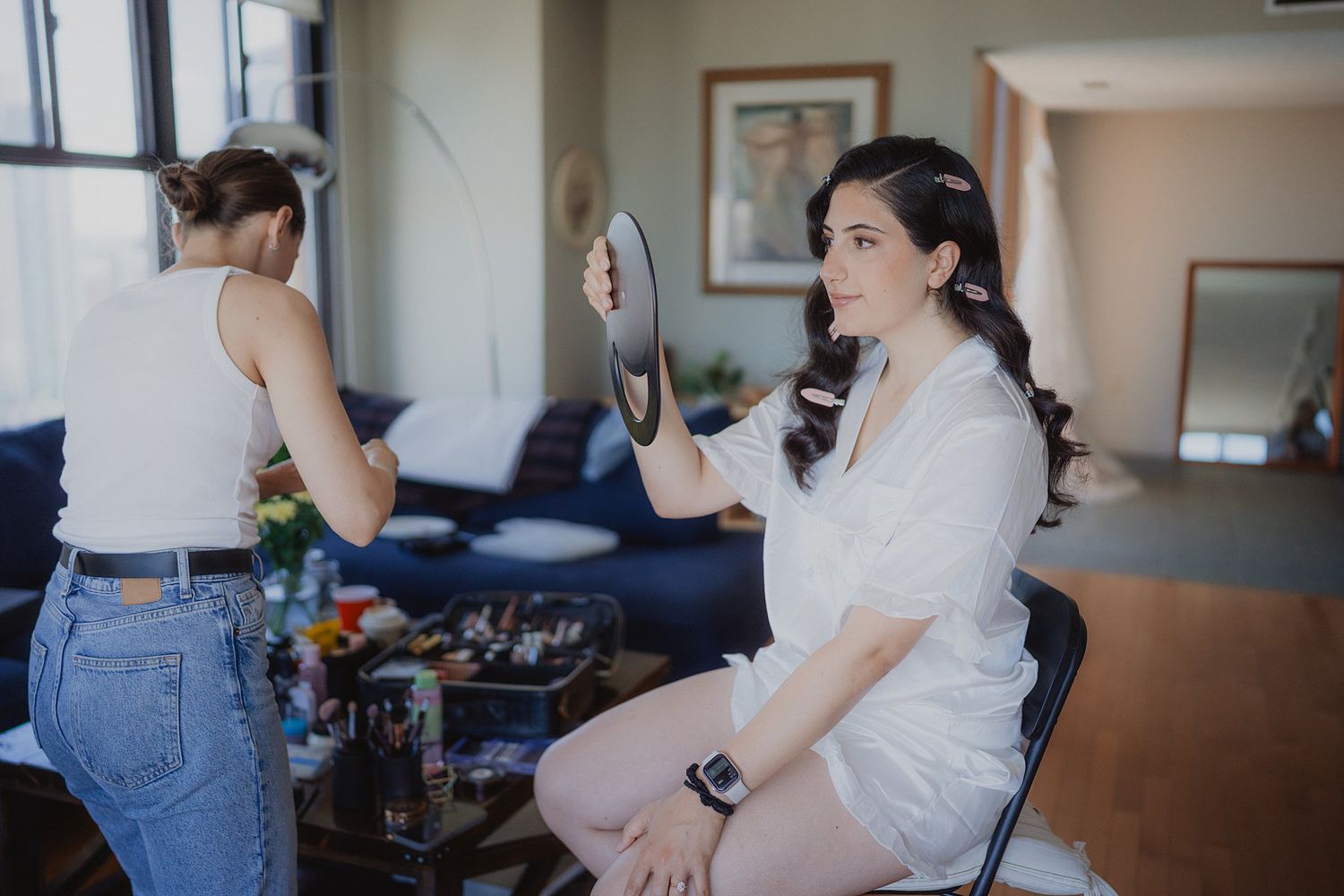 Wedding party getting ready in a bright modern room with white dresses and floral arrangements.