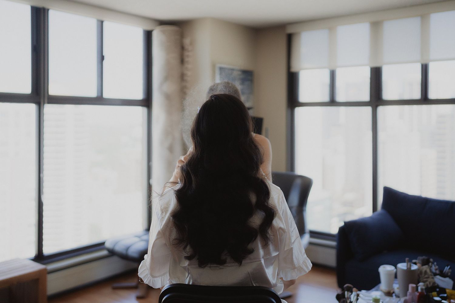 Long dark hair silhouette against bright windows in modern apartment room.