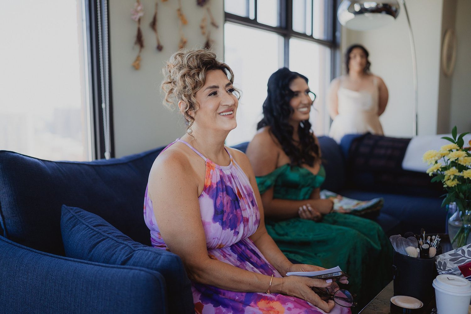 Wedding party members in purple dresses gathered on a blue couch in a bright room.