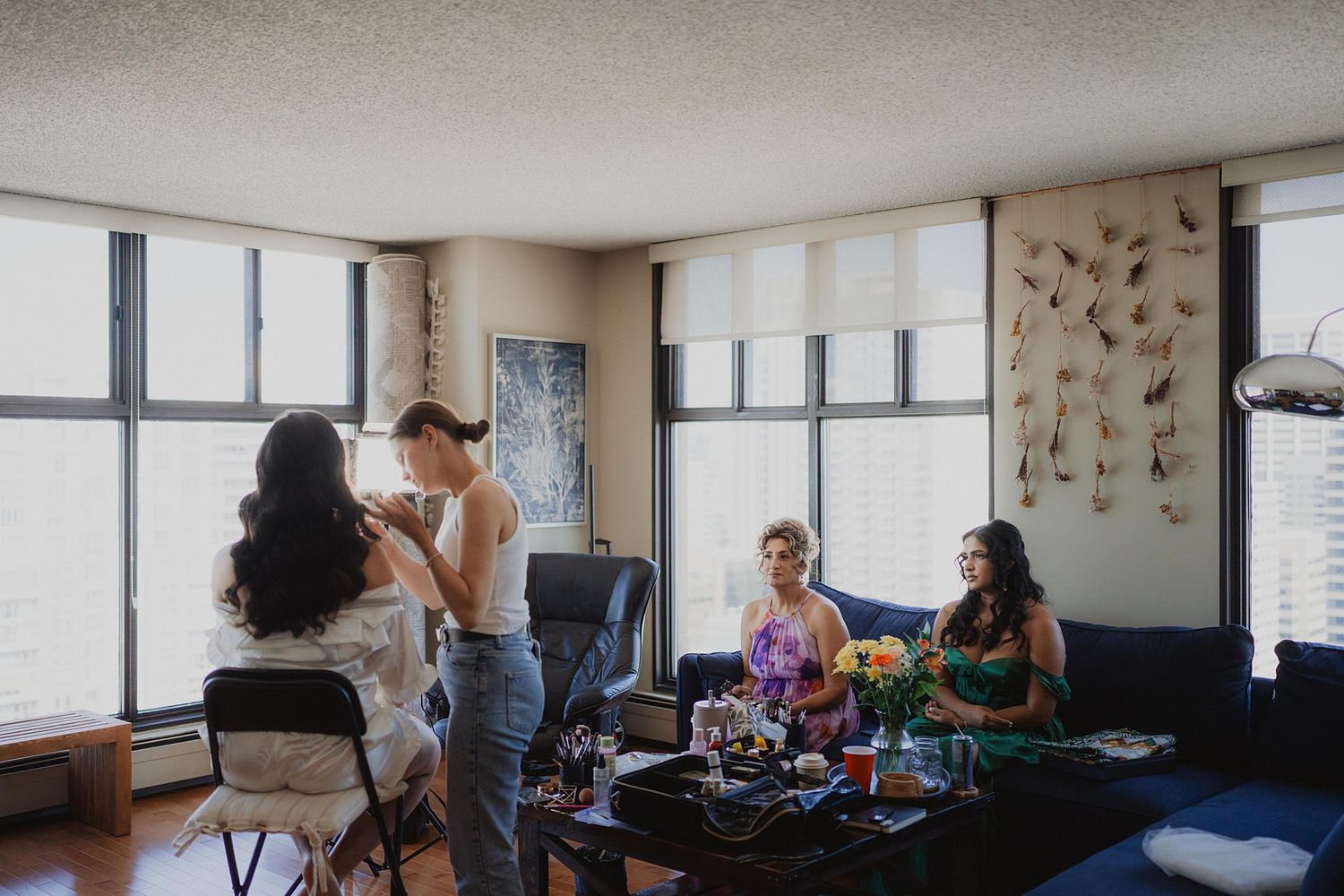 Wedding preparation scene in living room with makeup artists working and friends relaxing.