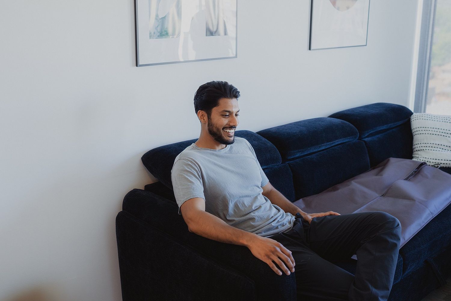 Person relaxing on a navy blue couch in a minimalist room with large windows.
