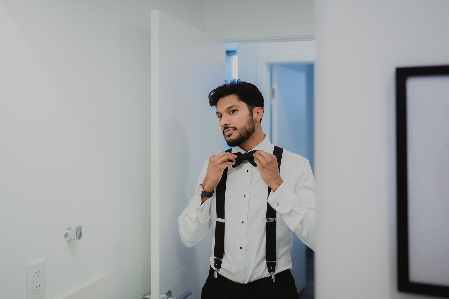 Person adjusting formal wear in front of white walls with minimalist artwork.
