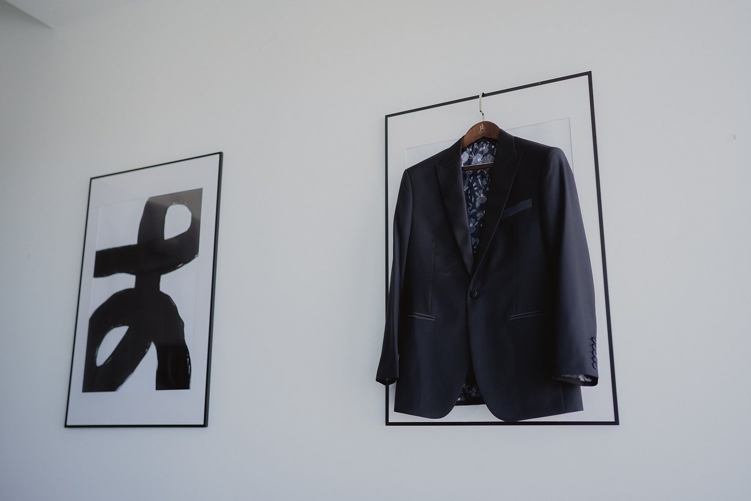Black formal suit jacket hanging on display next to modern wall art in a minimalist setting.