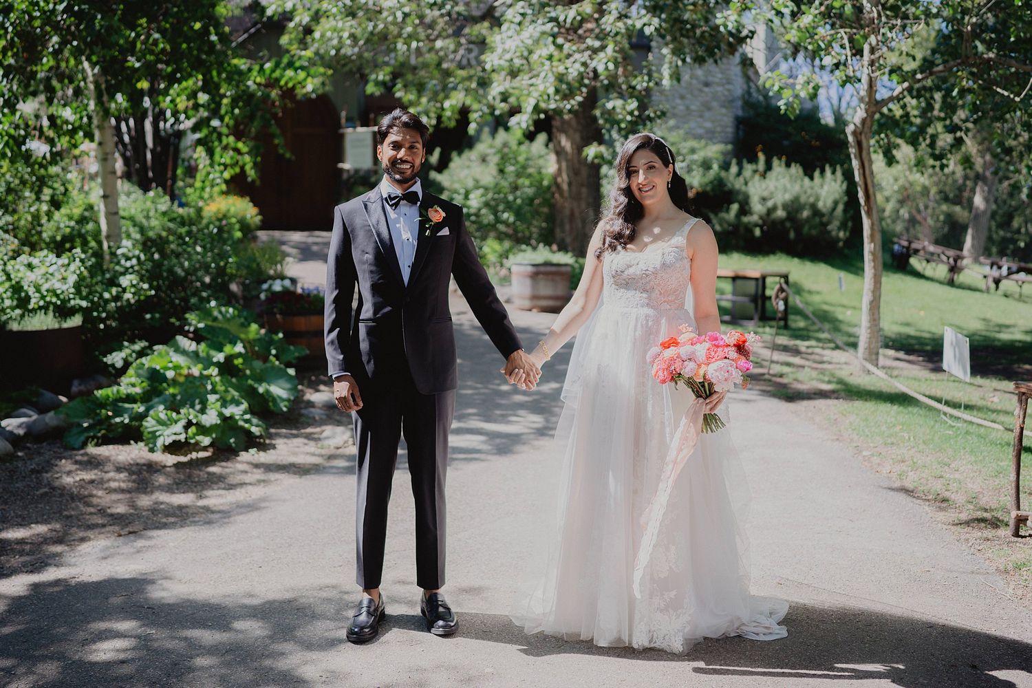 Newlyweds walking together along a tree-lined garden path after their ceremony.