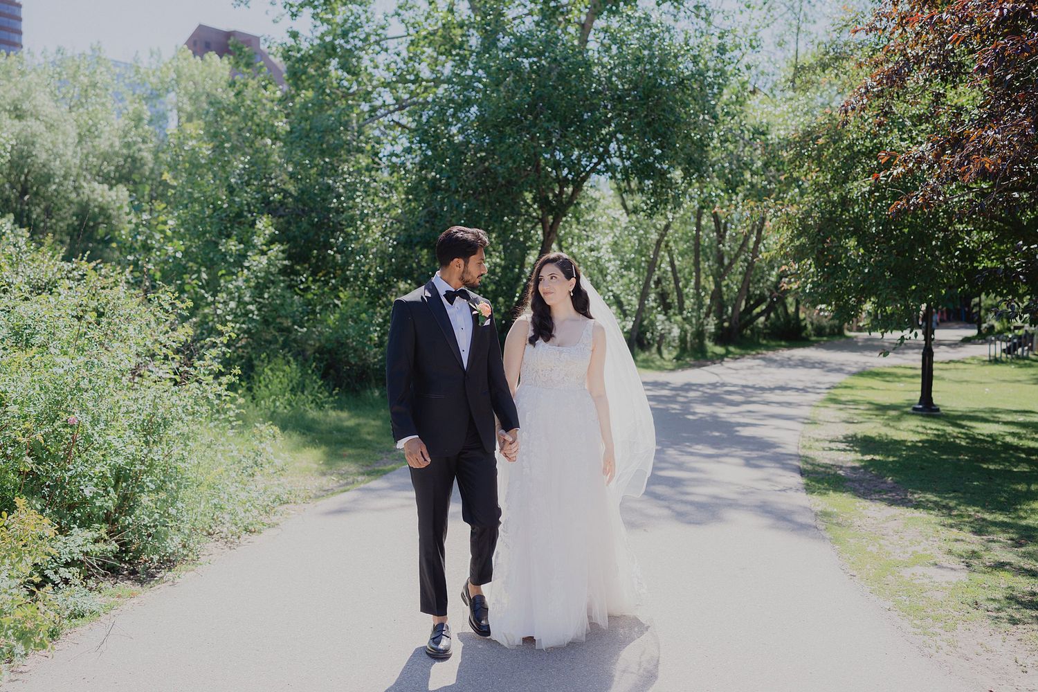 Wedding couple walking along a tree-lined path on a sunny summer day.