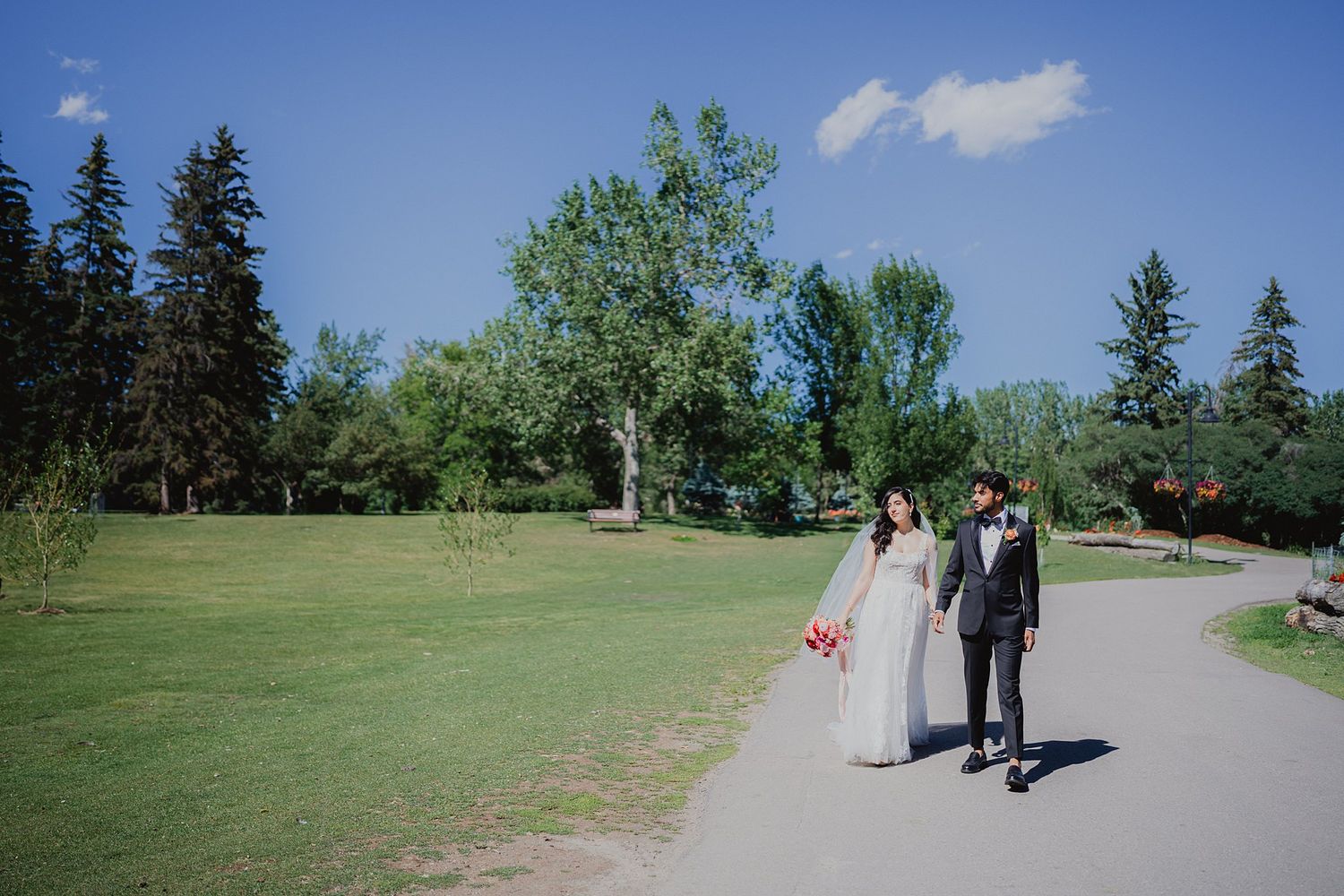 Wedding party walking along a scenic pathway with evergreen trees and blue skies.