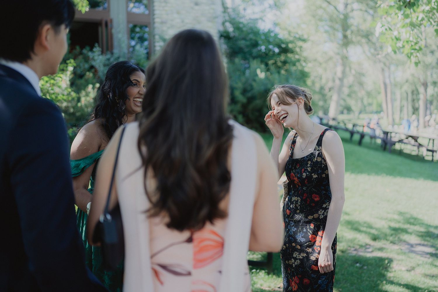 Candid wedding party moments captured in a sunlit outdoor garden setting with natural foliage.