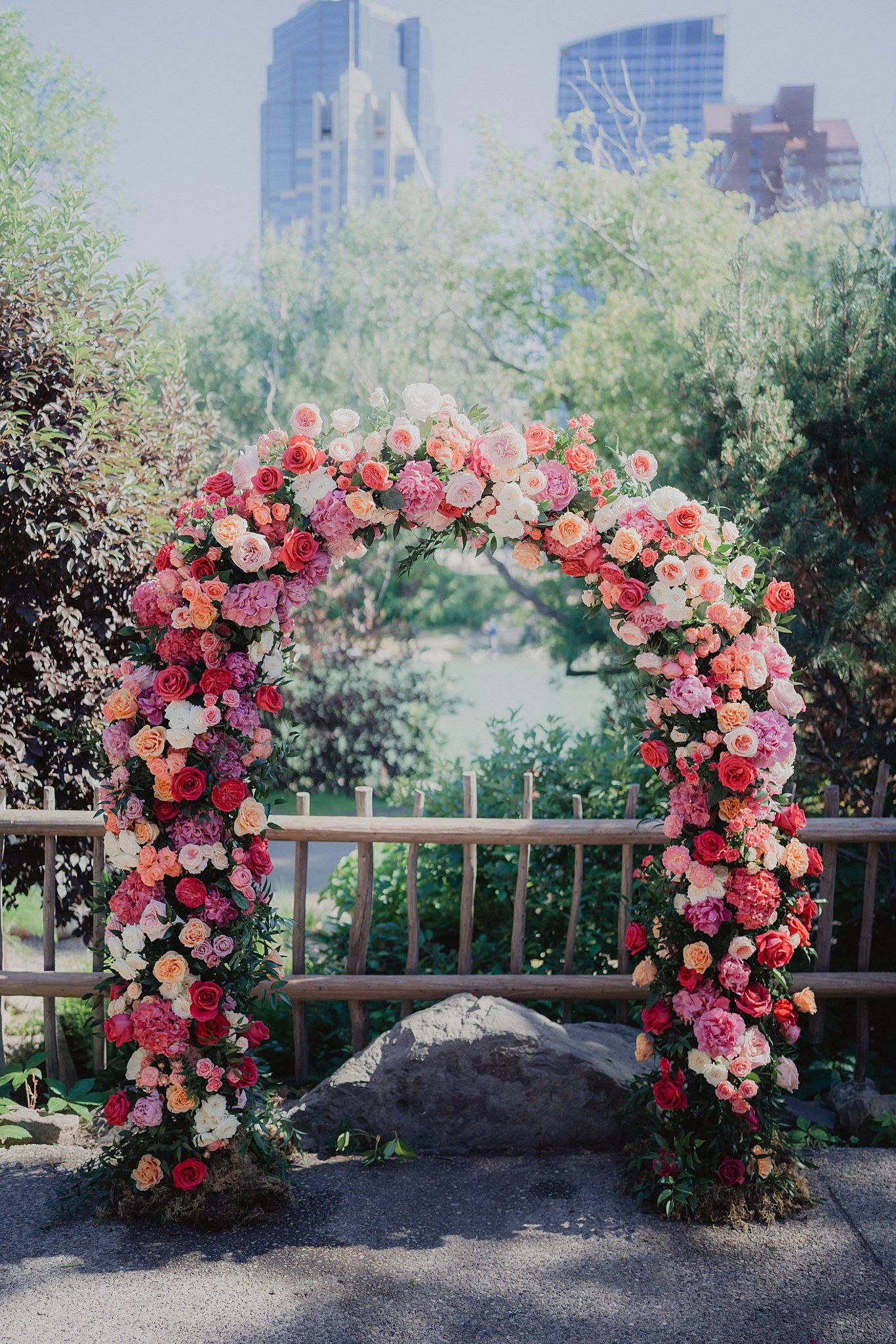 Beautiful floral arch with pink and red roses against a city skyline backdrop.