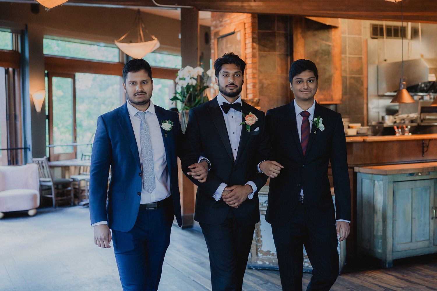 Groomsmen in coordinated suits gathered in a rustic indoor venue.
