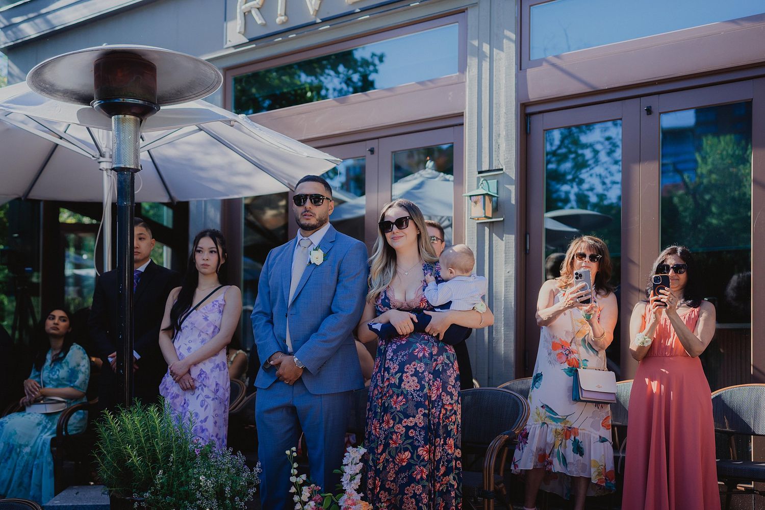 Wedding guests enjoying a celebration under white umbrellas at an outdoor reception venue.