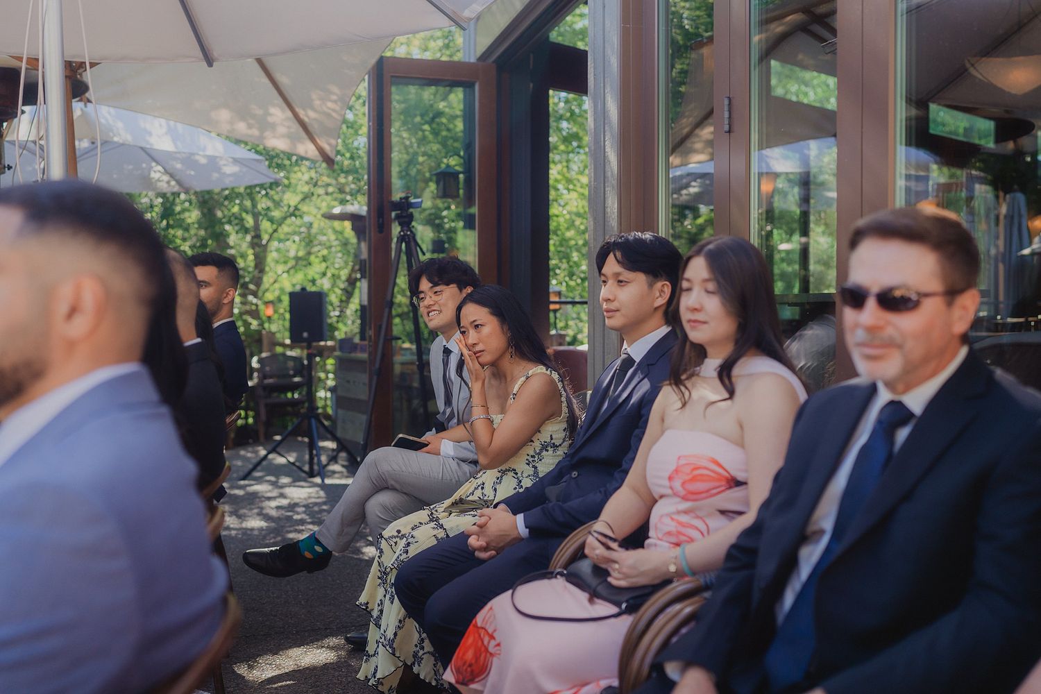 Wedding guests seated at outdoor covered patio tables during a daytime reception.