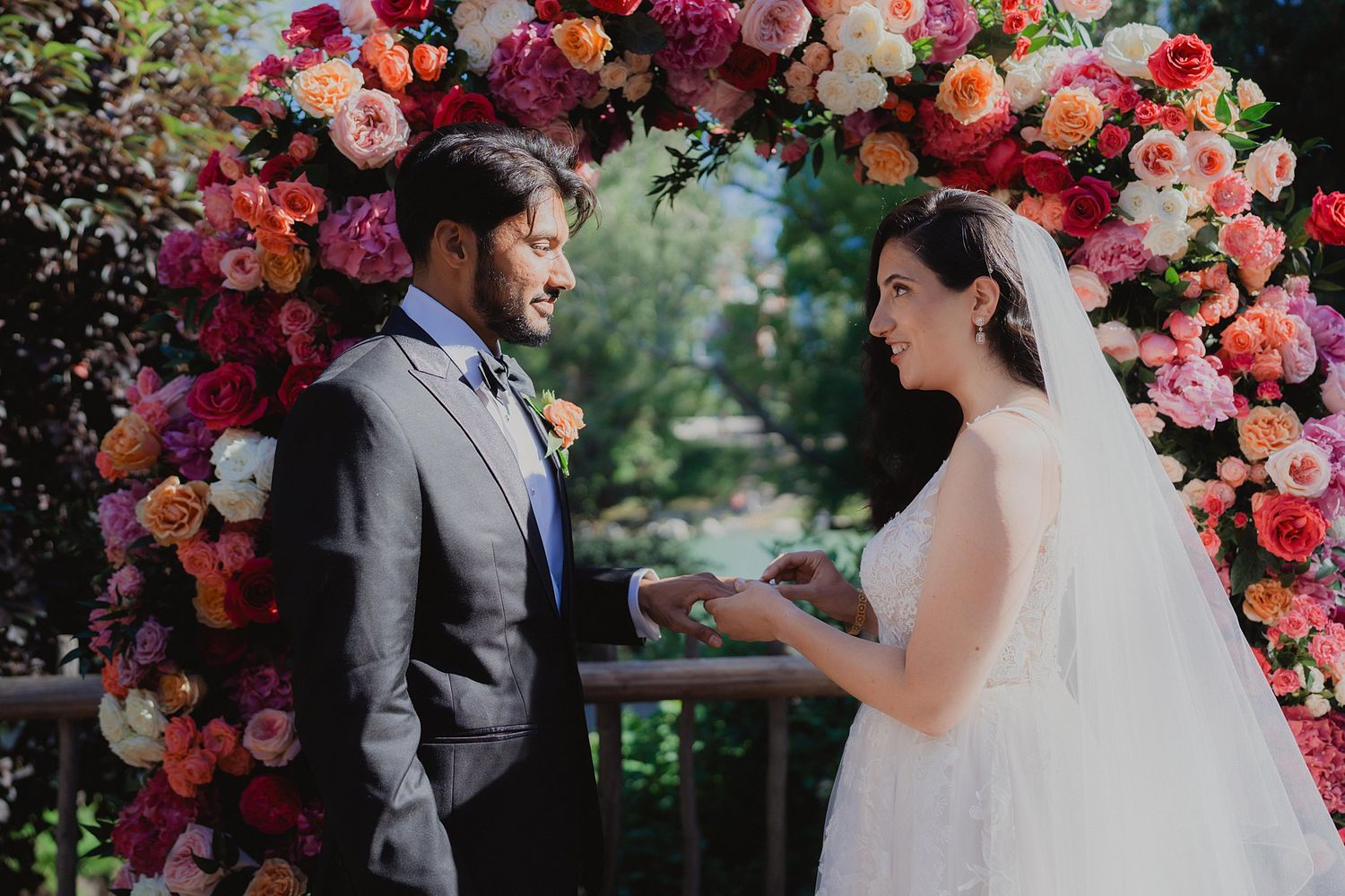 Couple shares intimate moments near a lush floral arch with pink and coral blooms.