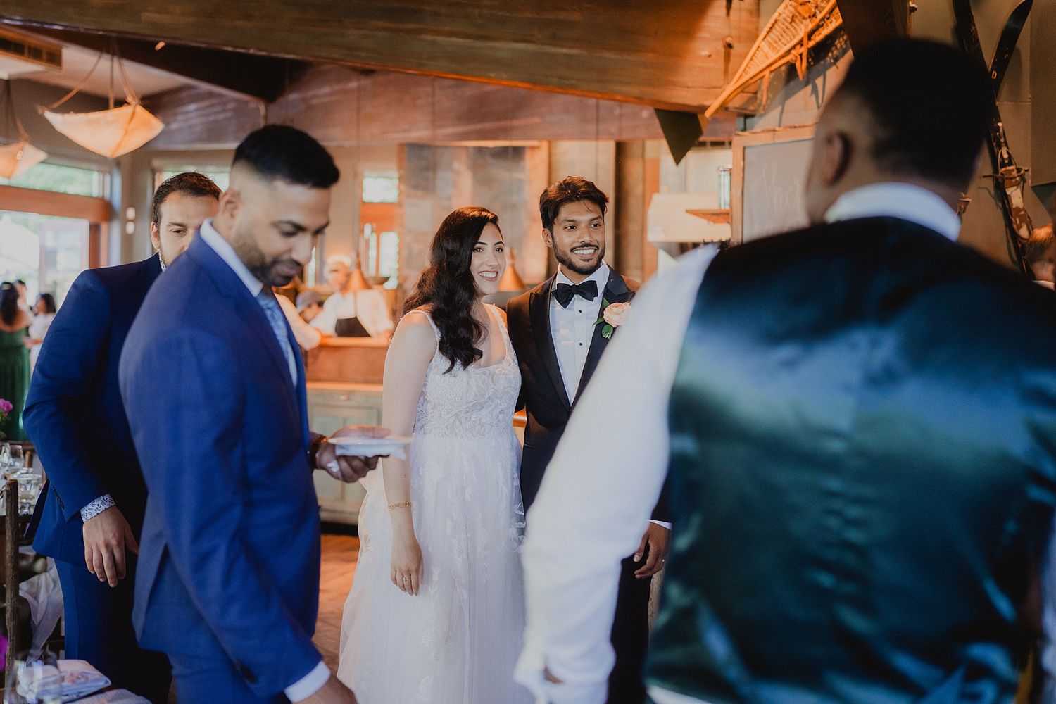 Wedding party in blue and white attire gathered in a warmly lit rustic venue during celebration.