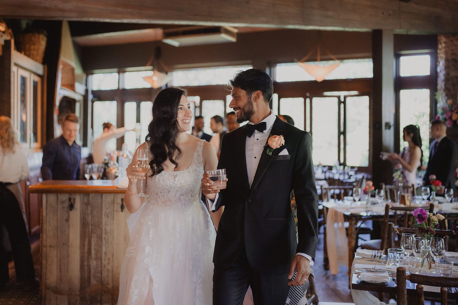 Wedding reception guests celebrate joyfully in a rustic wooden venue with warm lighting and decorative details.