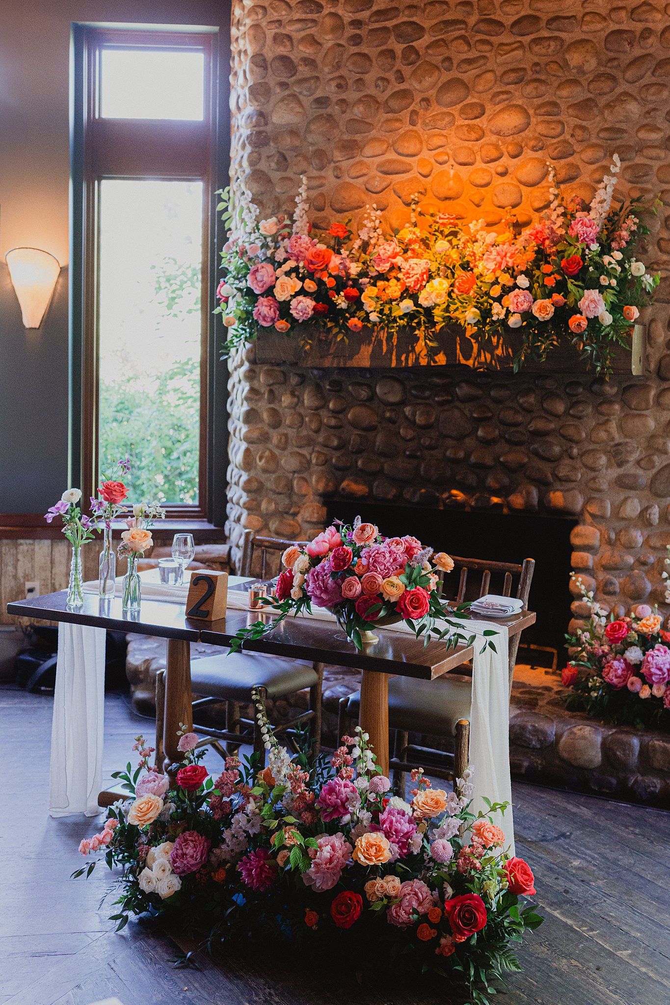 Elegant floral arrangements with pink roses decorate a rustic stone wall venue.