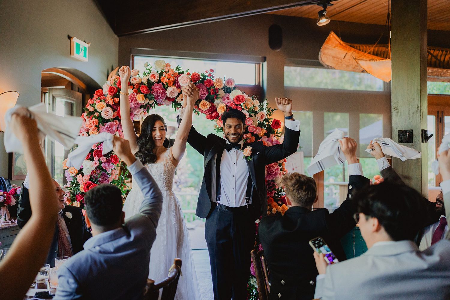 Wedding guests celebrate with raised arms during joyful reception moment.