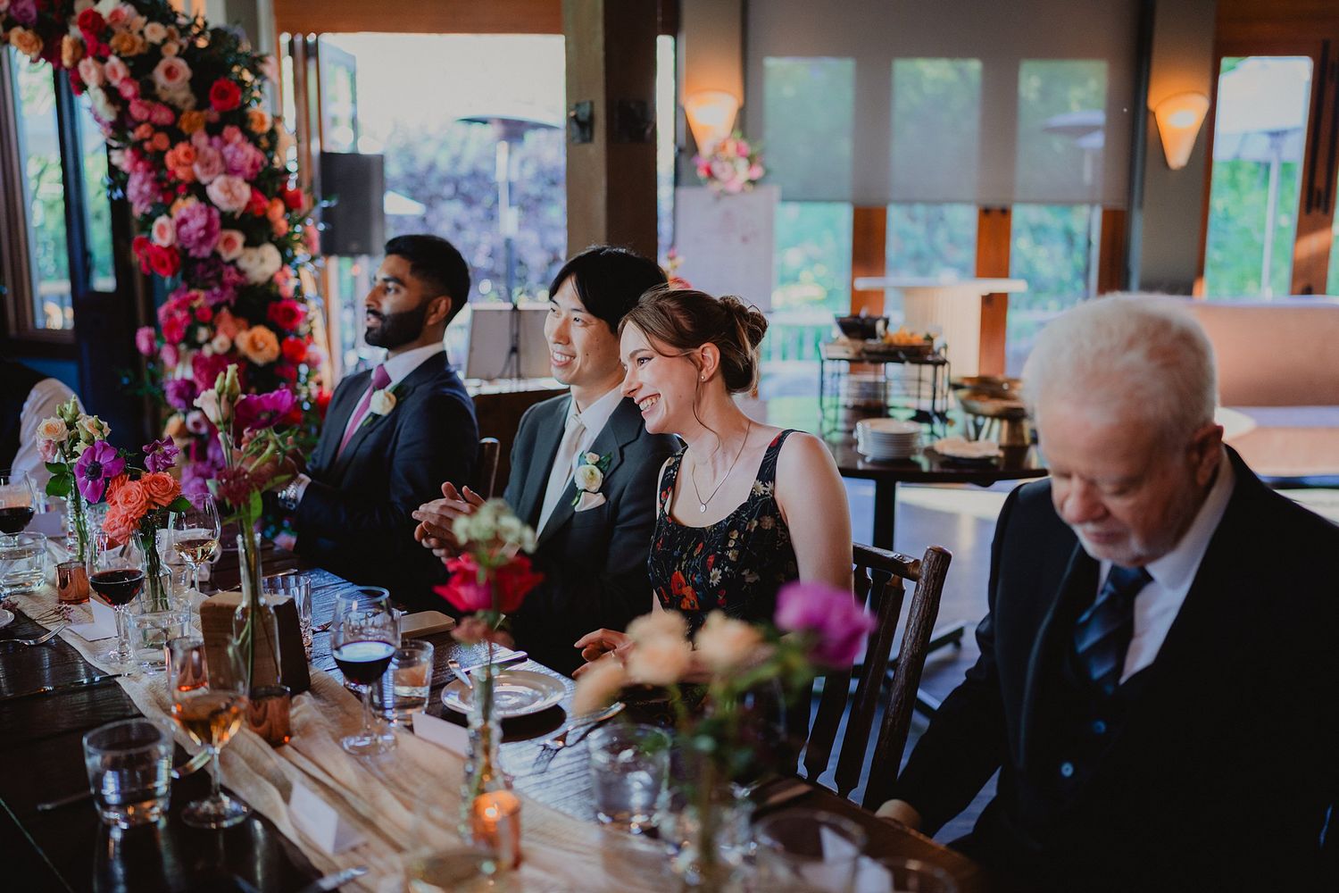 Guests seated at dining tables during an indoor event with pink floral decorations and natural lighting.