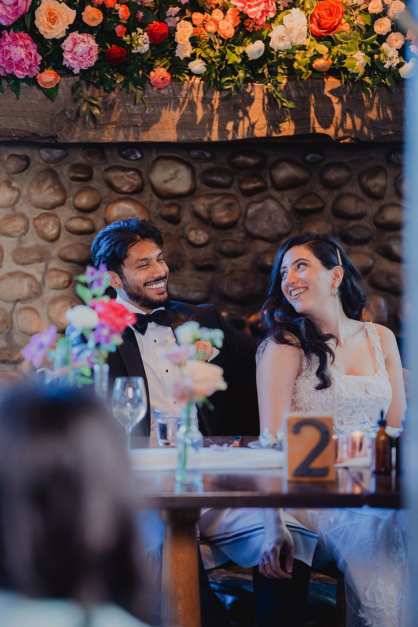 Newlyweds share a moment at their reception table decorated with vibrant floral arrangements.