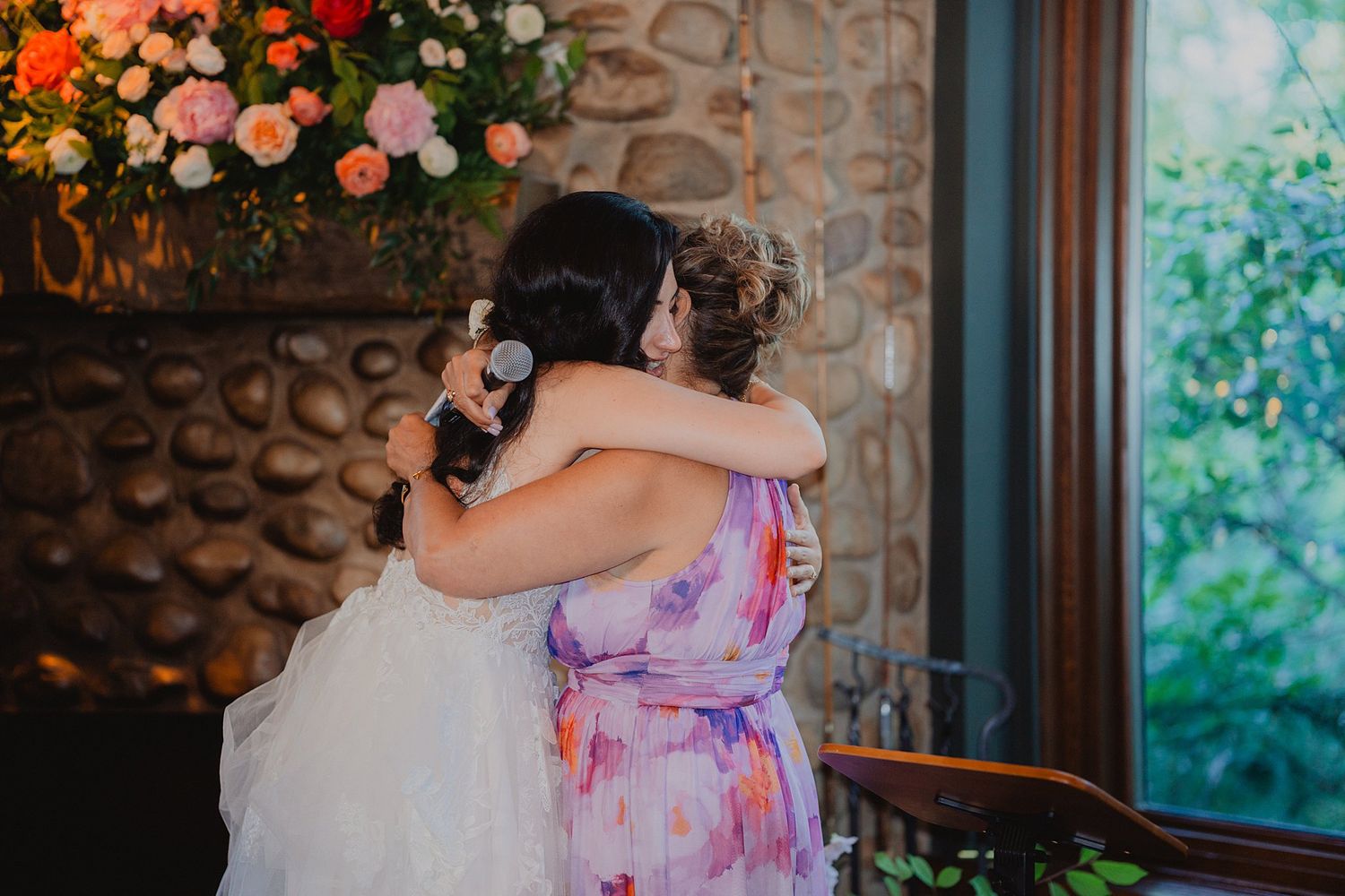 Wedding reception decor features vibrant pink and orange floral arrangements against stone walls.