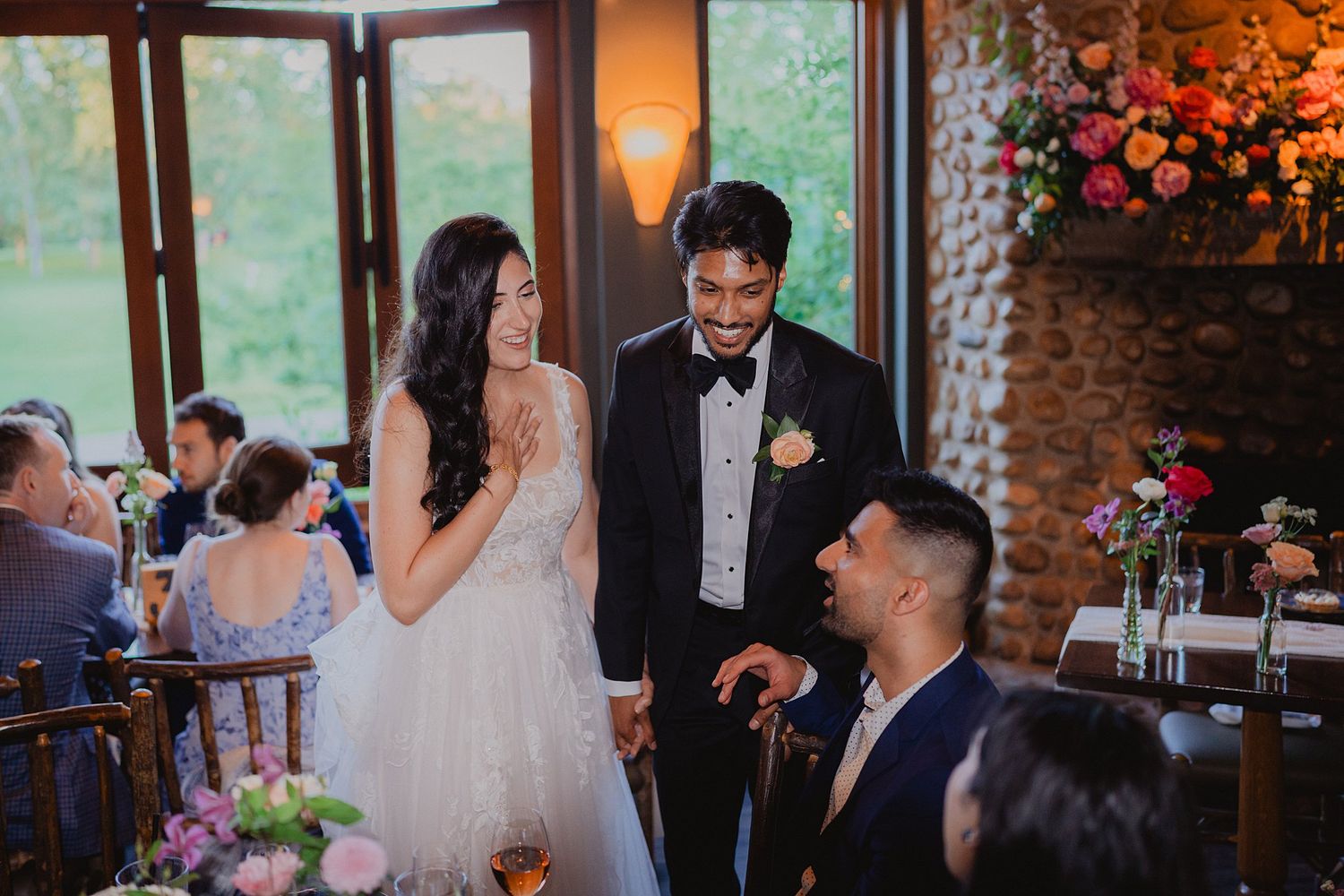 Indoor wedding reception venue with warm lighting, floral arrangements and large windows overlooking greenery.