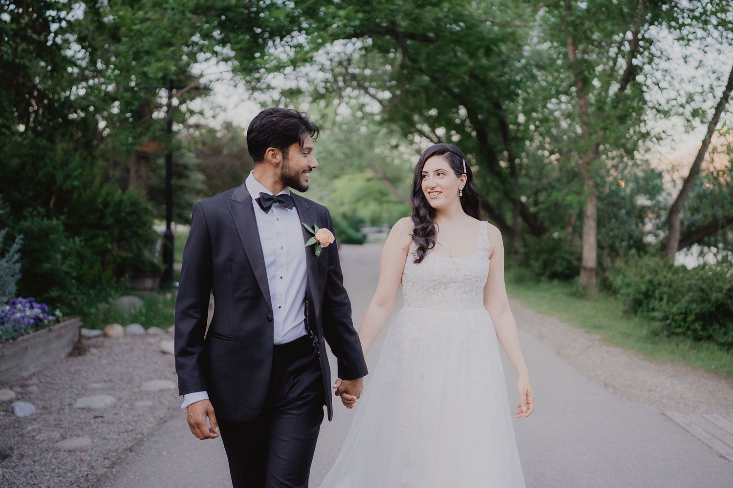 Couple walking together on a tree-lined path during a wedding photo session.