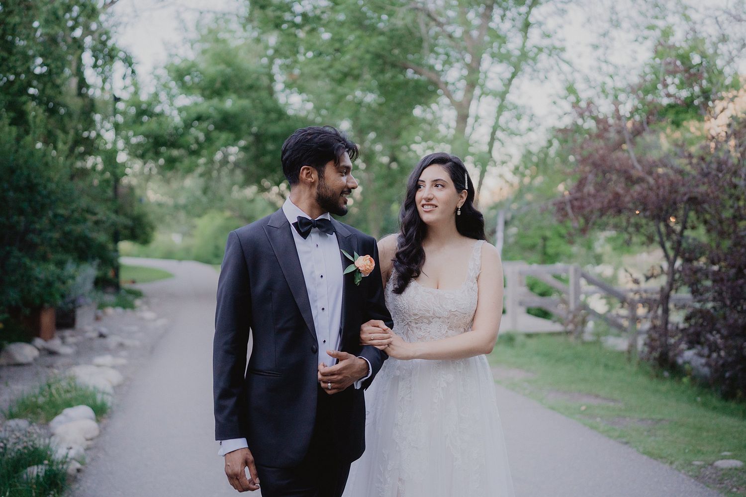 Couple poses for romantic wedding photos on a tree-lined path in springtime.