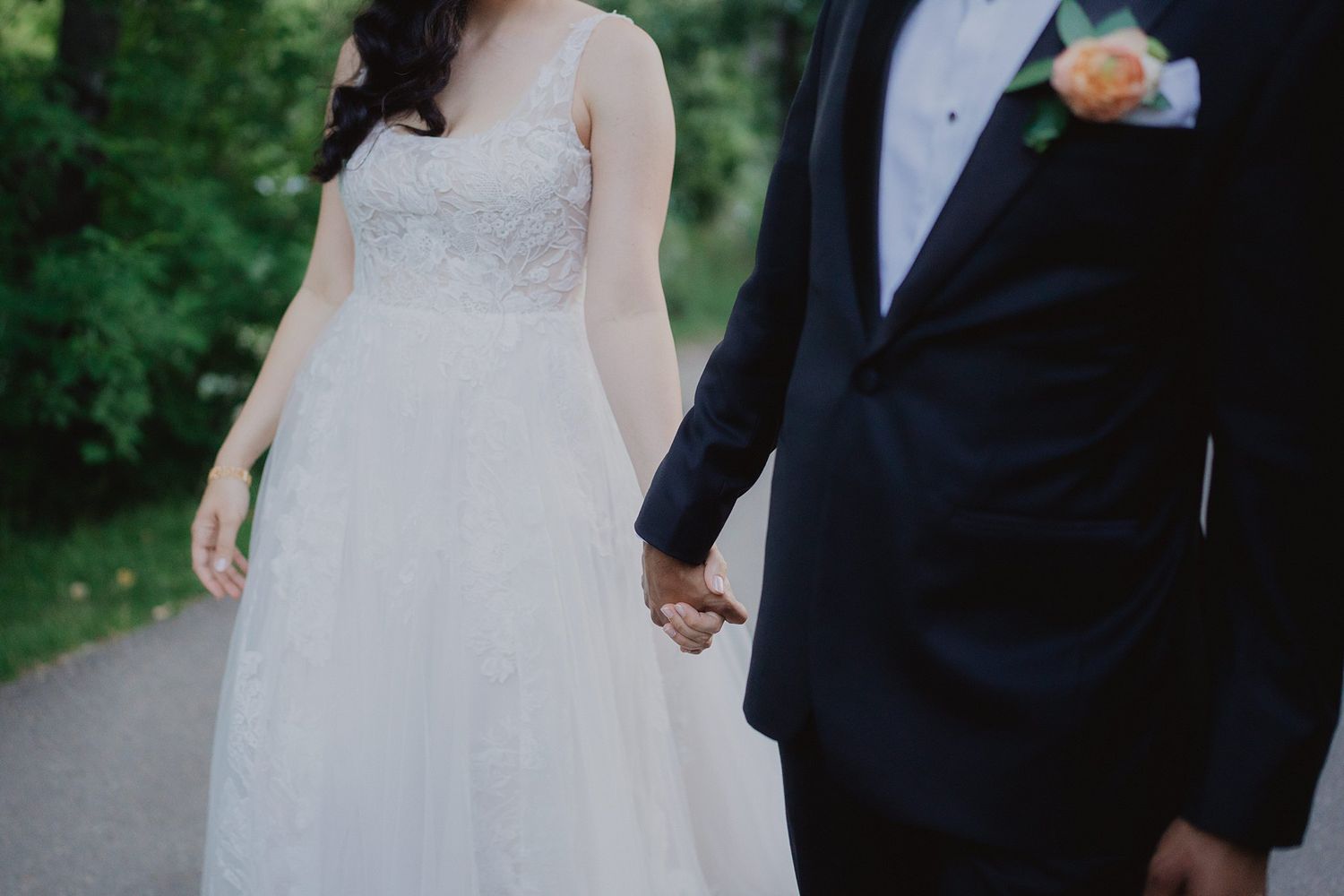 Wedding couple photographed from shoulders down showing formal attire outdoors.
