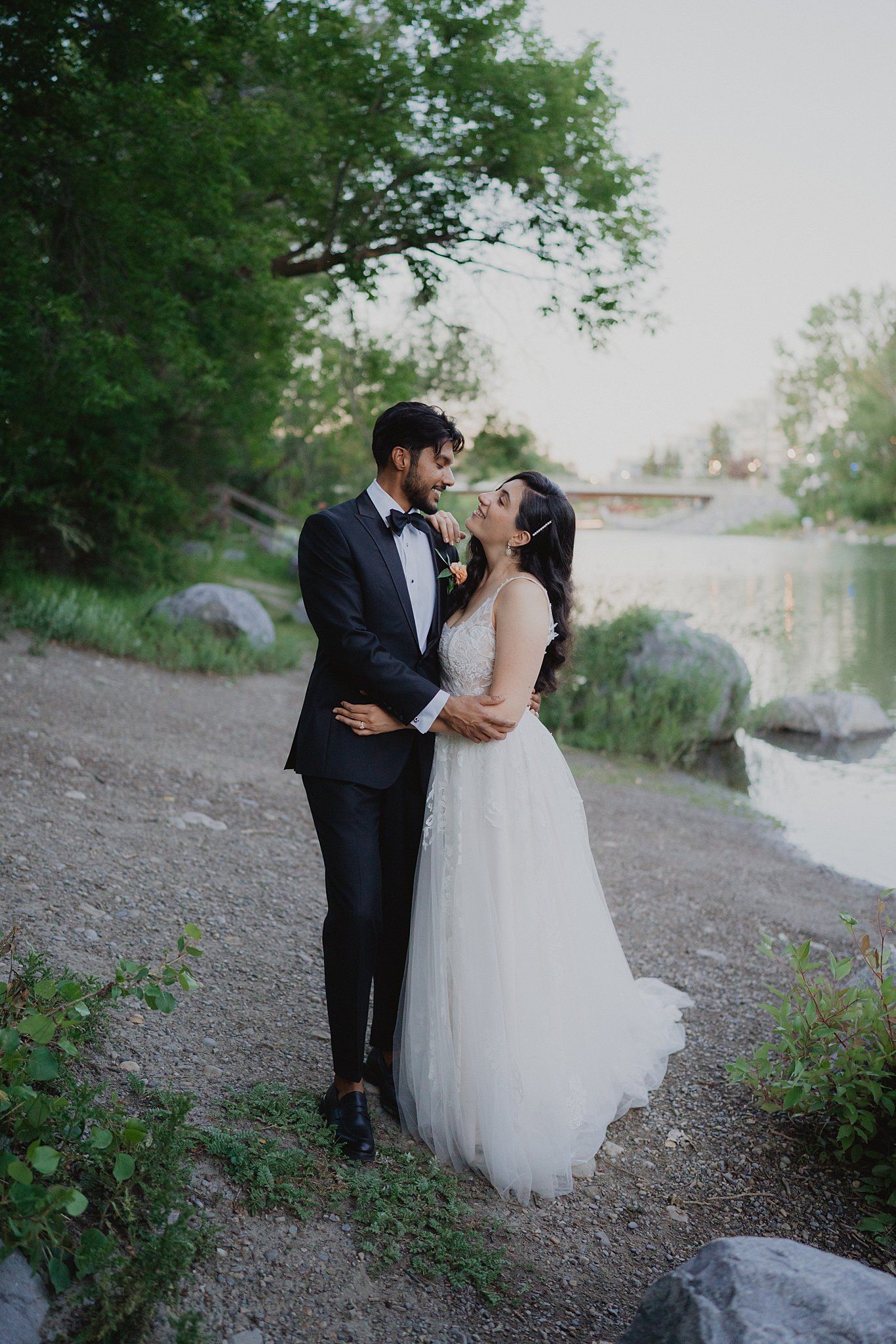 A romantic wedding couple shares intimate moments on a scenic outdoor path surrounded by greenery.