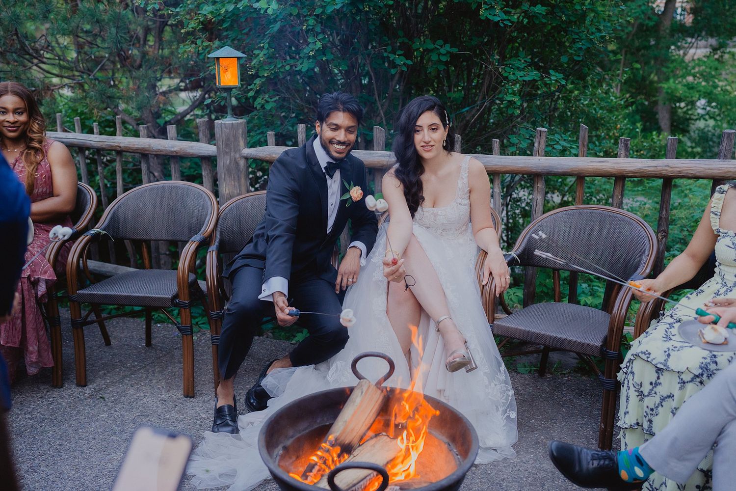 Wedding guests gather around a cozy fire pit during an outdoor reception celebration.