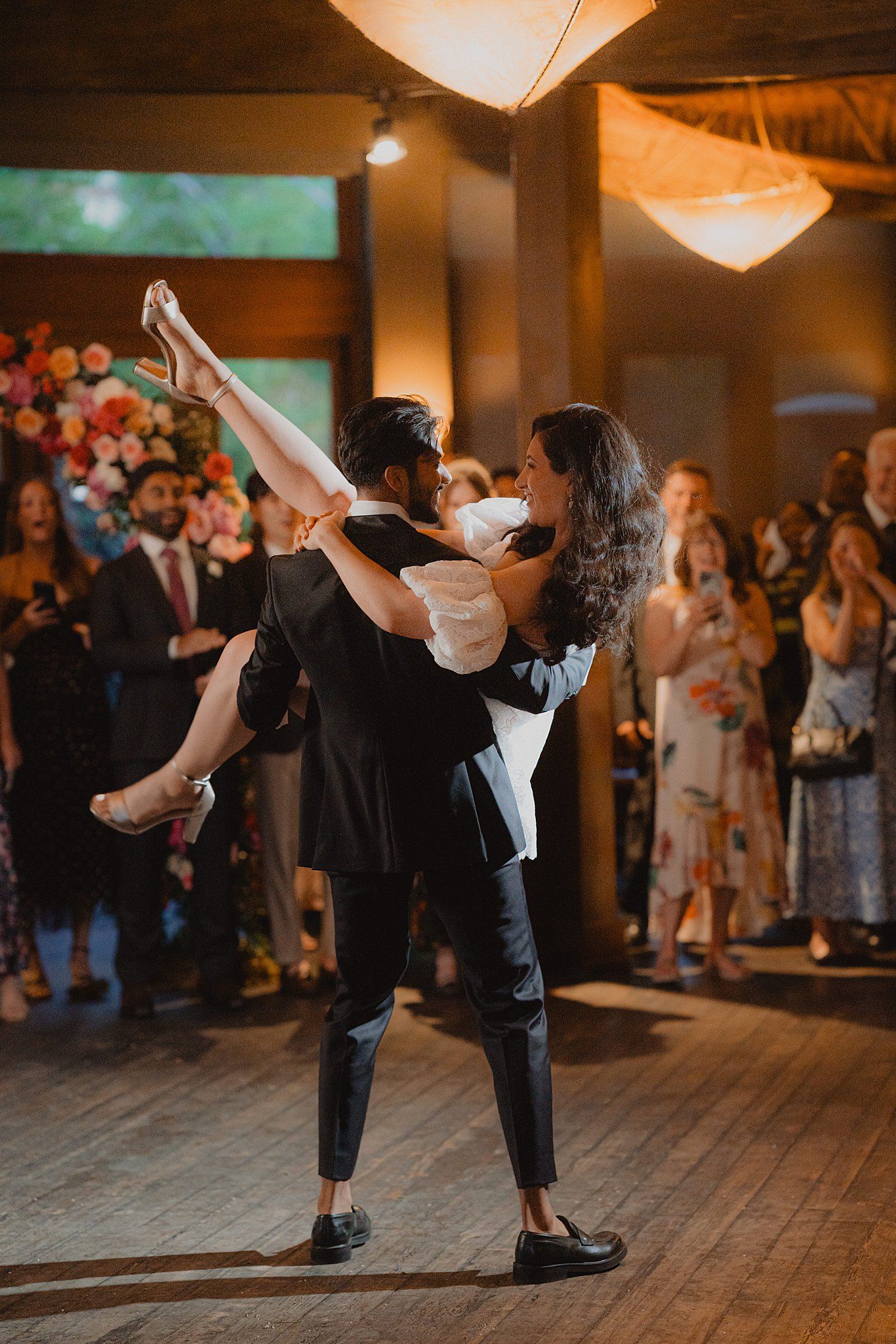 Wedding couple performs romantic dance moves on wooden floor during reception.