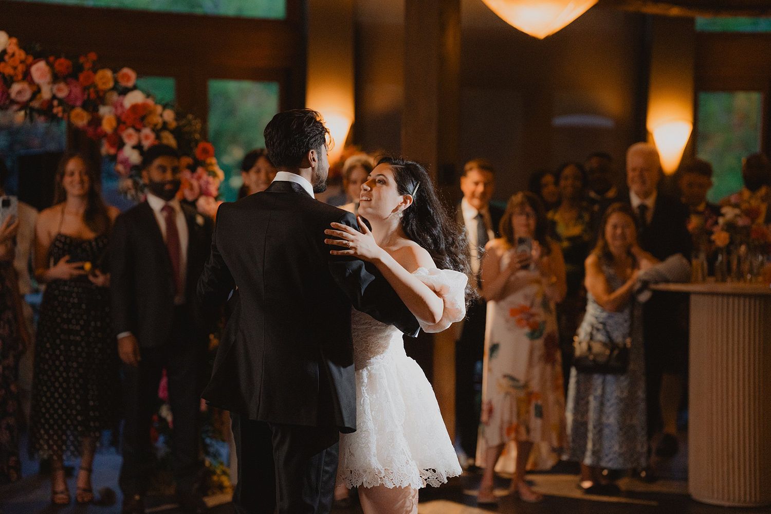 A romantic first dance moment at a wedding reception with warm lighting and guests watching in the background.