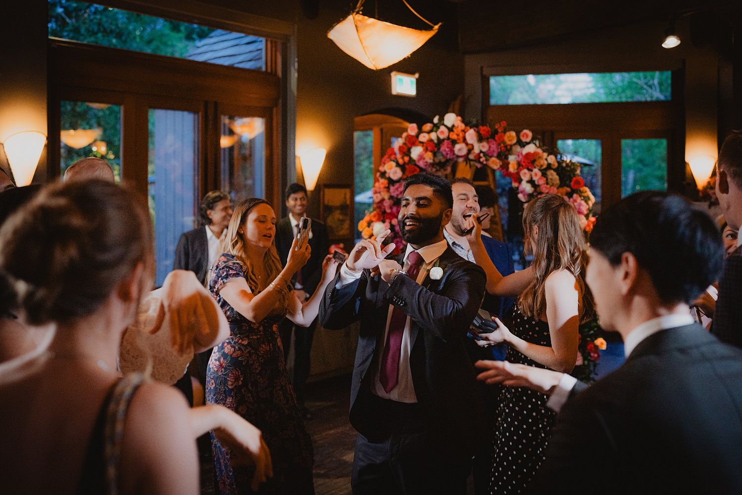 Wedding celebration in full swing with guests dancing under decorative lighting and floral arrangements.