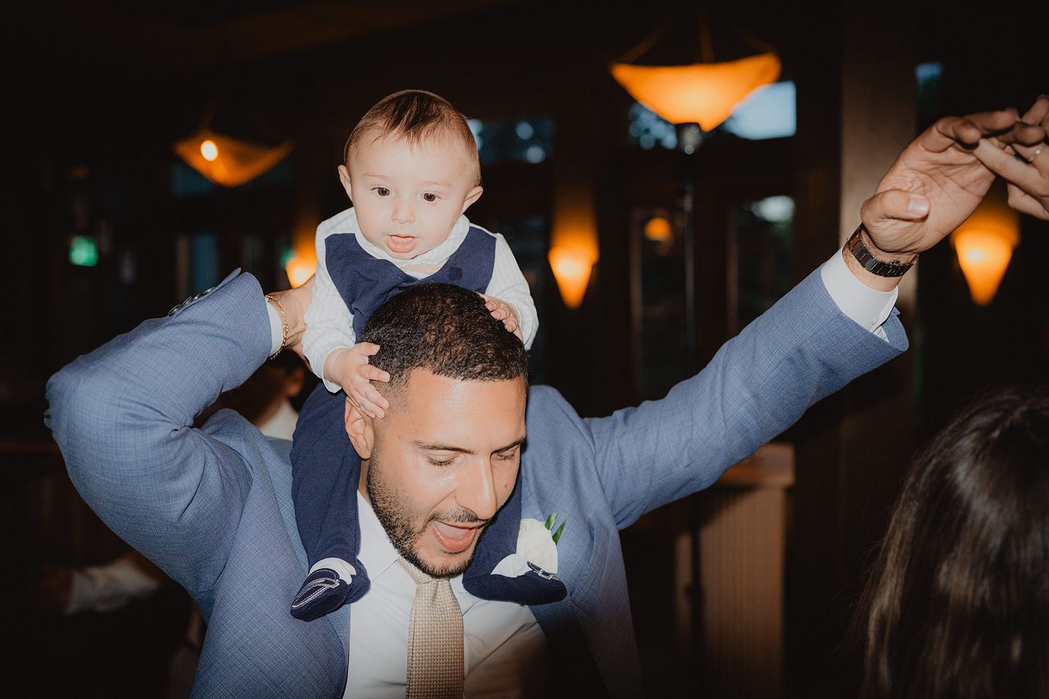 Sweet moment of a guest dancing with a baby at a dimly lit wedding reception.